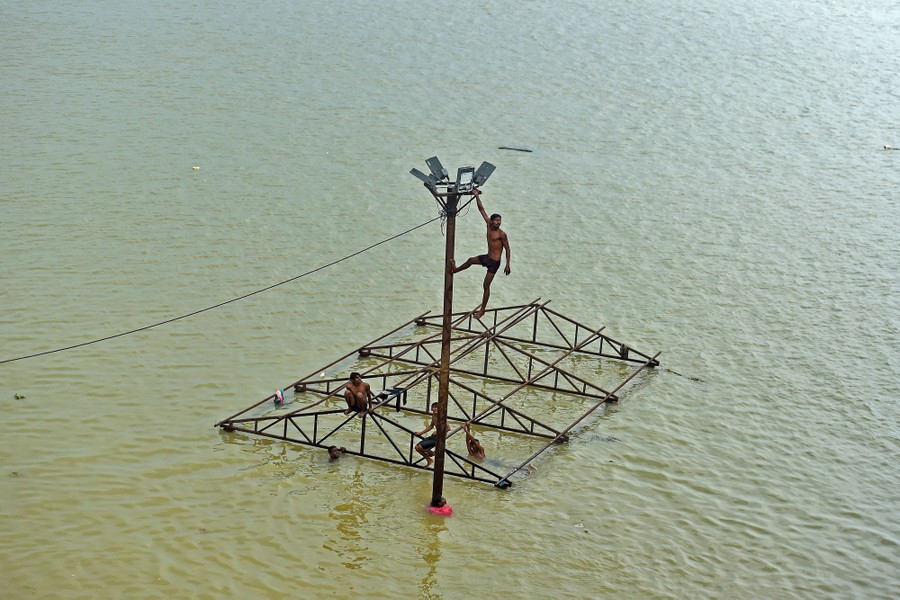 Several young men play on a structure submerged in a flooded river.