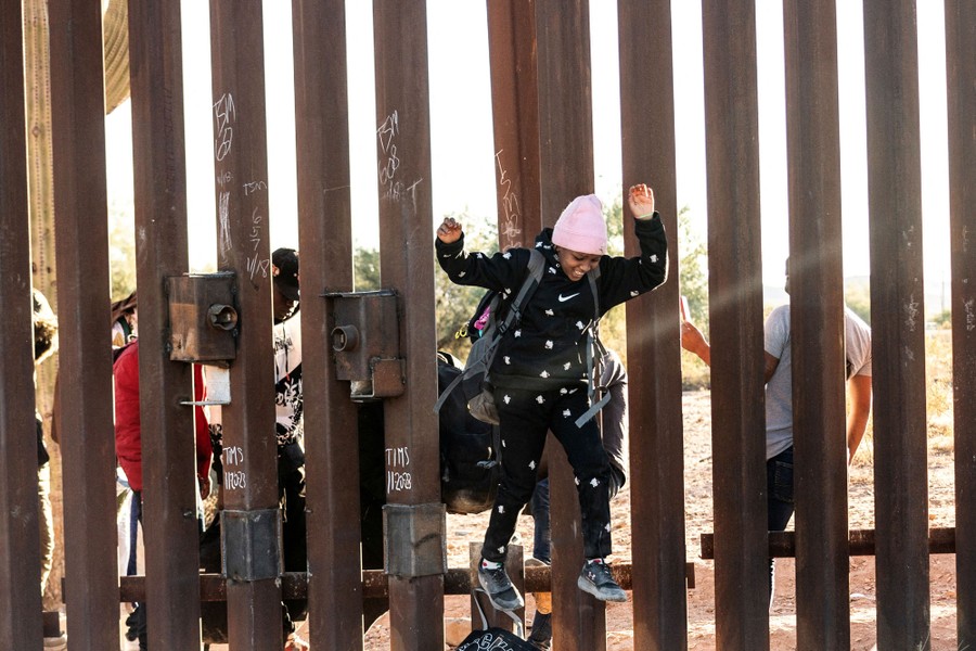 A child jumps through a hole in a border wall.