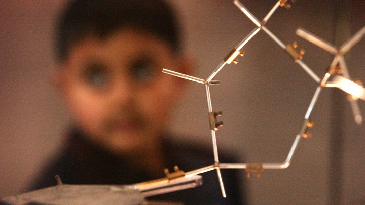 A boy stands behind a model of DNA.