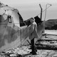 A black and white photograph of a man looking at a burned down home