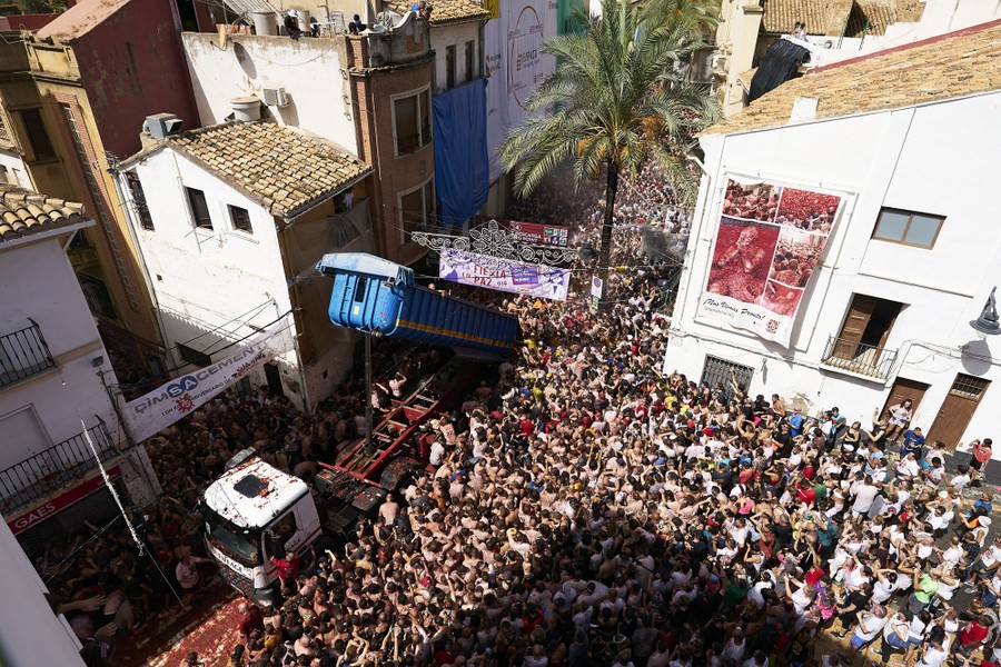 An elevated view of a dump truck tilted up, surrounded by a packed crowd of people in a plaza.