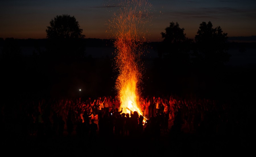 A crowd of people surrounds a tall bonfire at night.