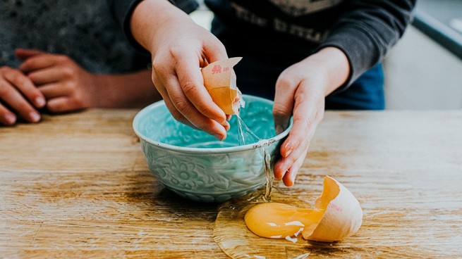 A person cracks an egg into a bowl