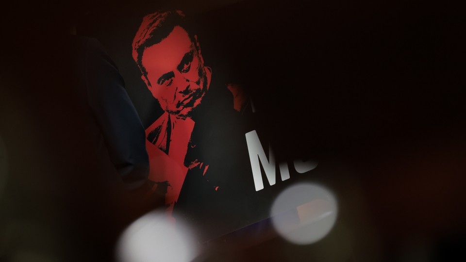 A color photograph of a poster of Elon Musk shown in a red gradient.