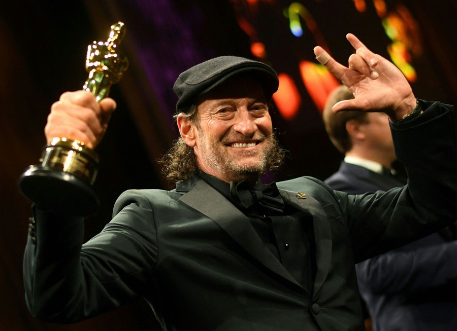 A man holds up his Oscar award while smiling.