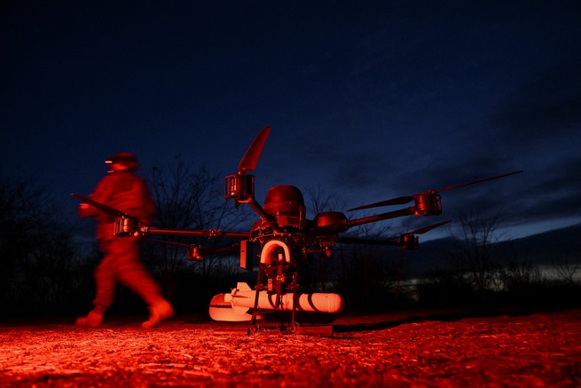 A drone in red light as a man walks behind it