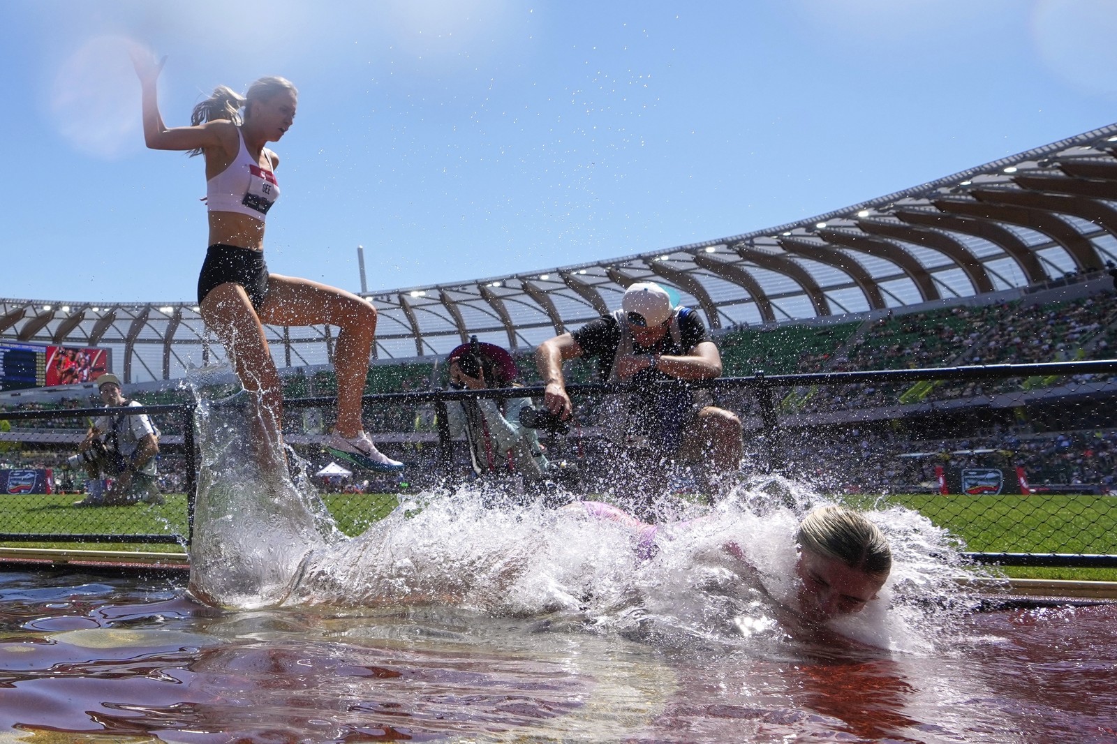 A runner stumbles and falls into a water obstacle during a race.