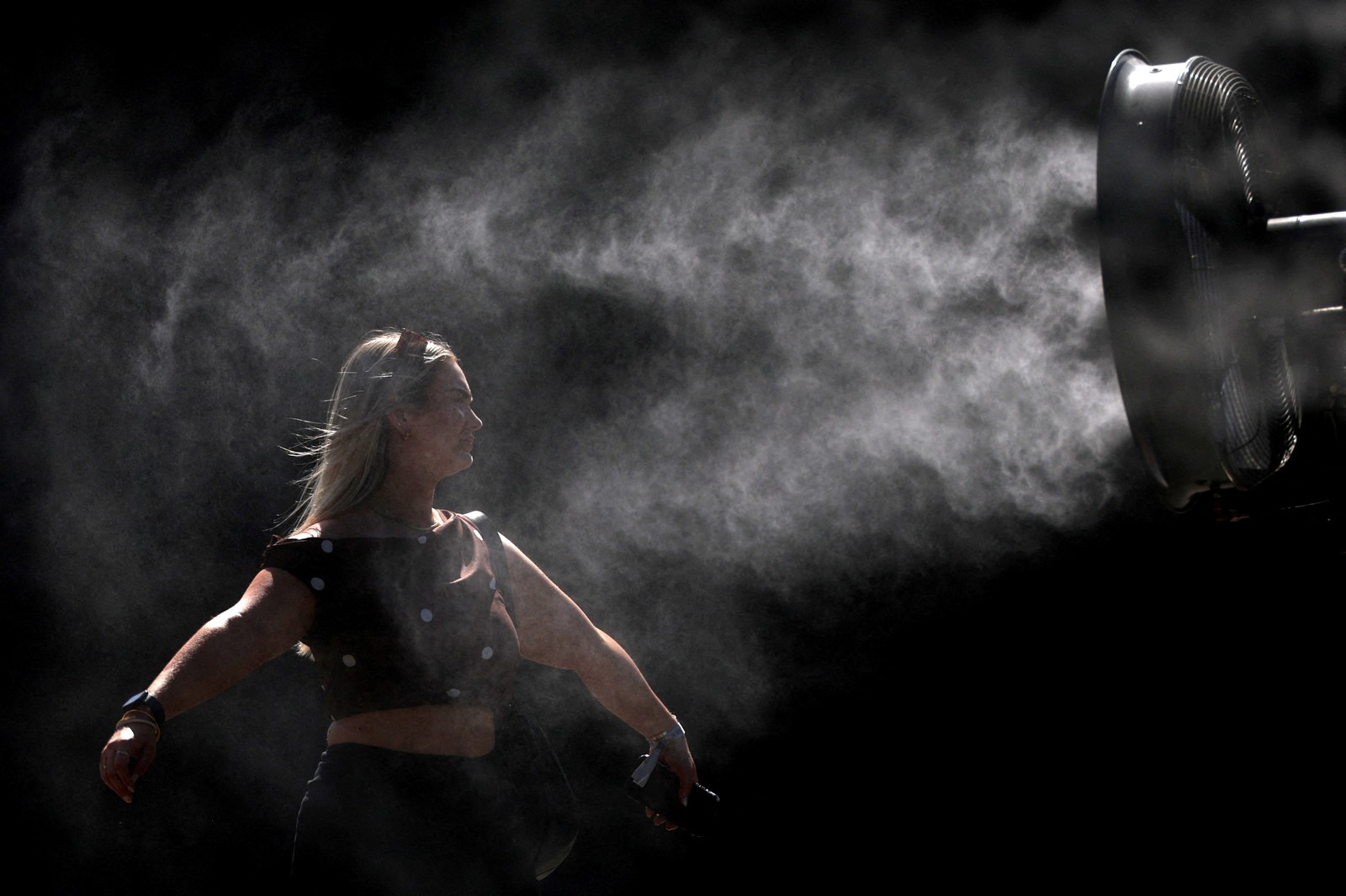 A woman cools herself down in front of a mist fan.