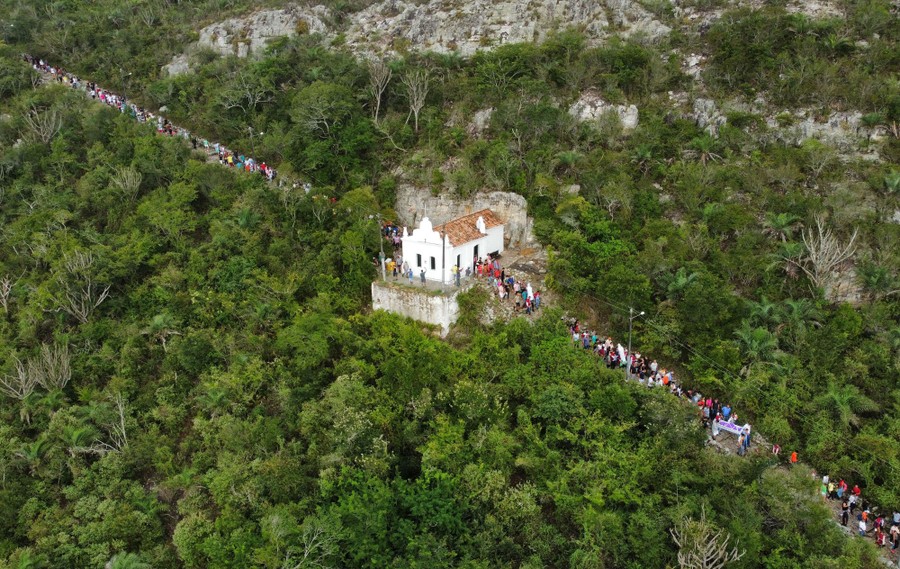 An aerial view of a chapel on a mountain path, with many people on the path