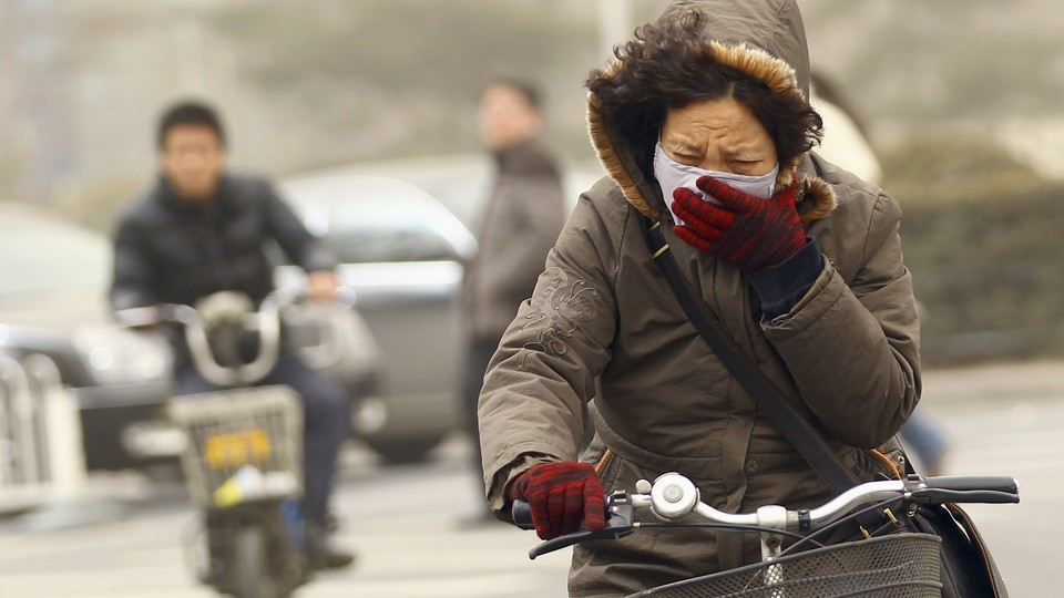 A woman covers her face while riding her bike.