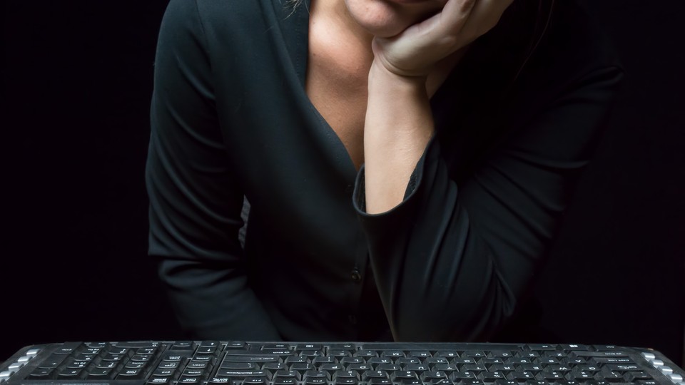 A woman rests her face on her hand while sitting in front of a computer keyboard.