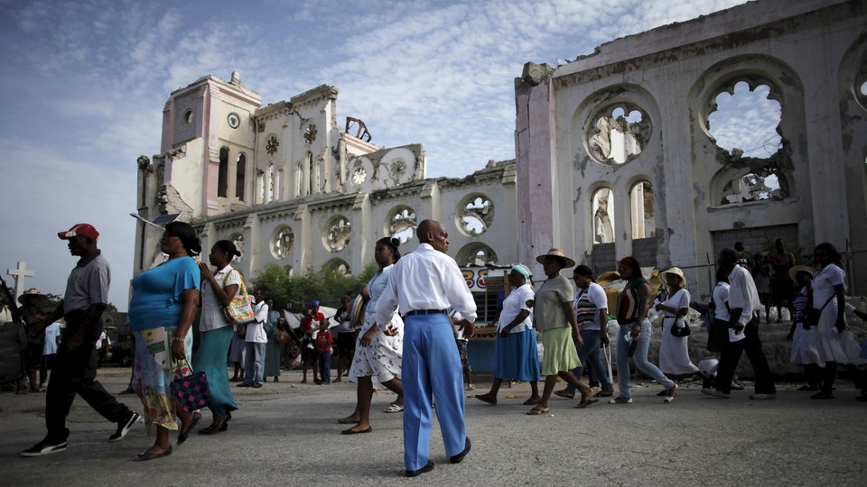 A procession walks past the ruins of the Notre-Dame de l'Assomption cathedral, destroyed in the 2010 earthquake.