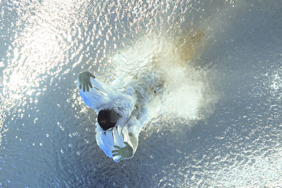 A view looking up from the bottom of a swimming pool, seeing a diver as they enter the water hands-first.