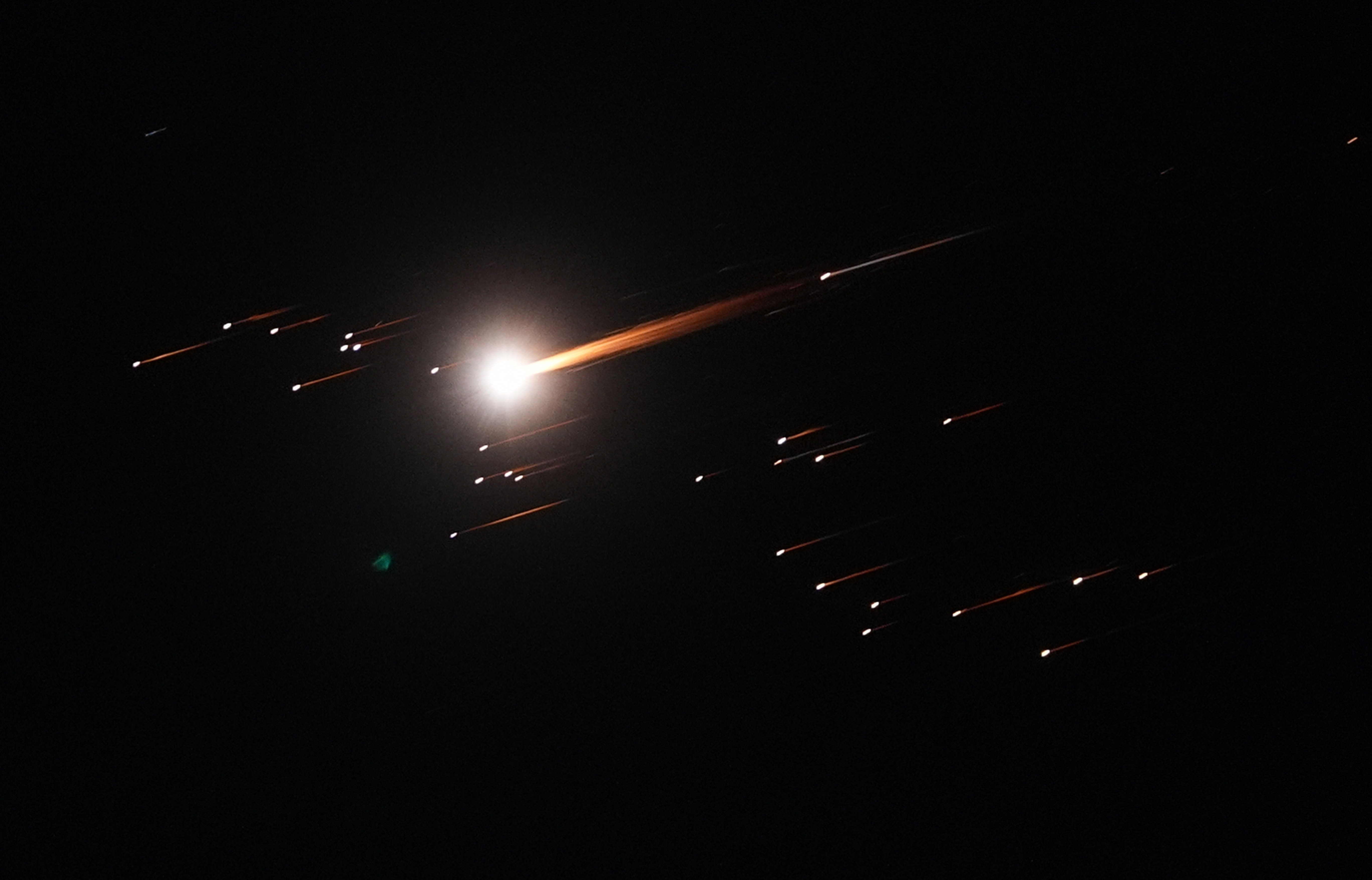 Many small and one large points of light streak across the night sky, missiles falling toward the ground.