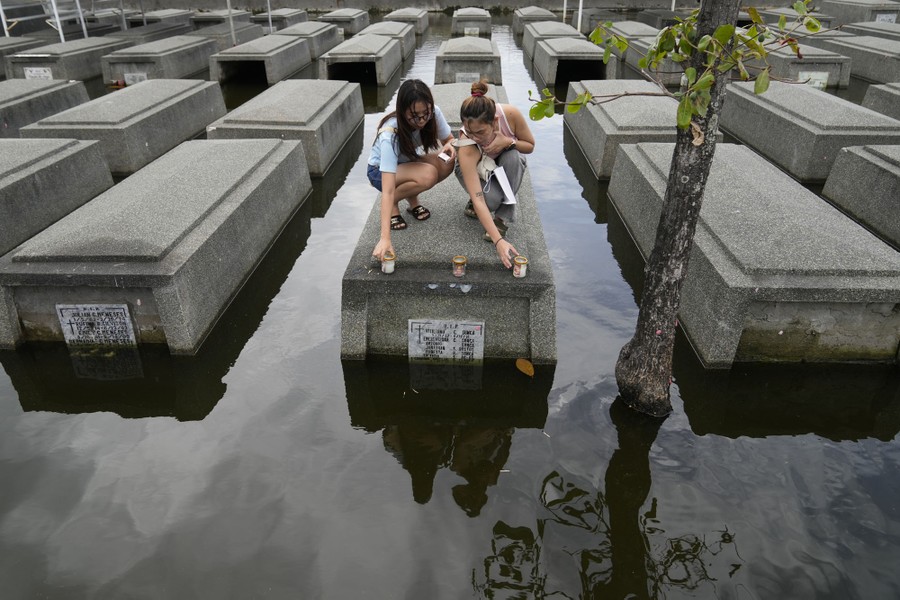 Two people kneel down to place candles on a tomb, surrounded by floodwater.