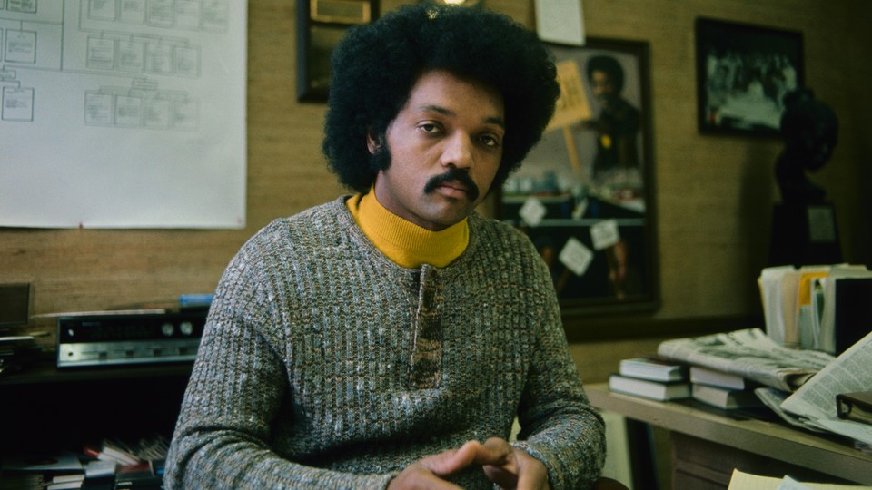 A color photograph of Jesse Jackson in his office wearing a yellow turtleneck