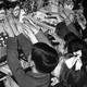 A black and white photograph of a gaggle of children reaching up onto a counter filled with boxes and jars of candy