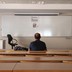 The back of a man sitting in an empty classroom, facing a blank dry-erase board
