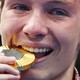 A close view of an athlete's face during a medal ceremony. He is playfully biting a gold medal, with tears falling from both eyes.