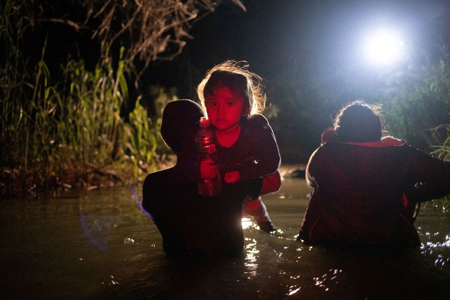 Several people wade through waist-deep water at night; one carries a small child.