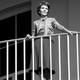 Nancy Reagan stands on a balcony, watching an unseen President Ronald Reagan depart the White House.