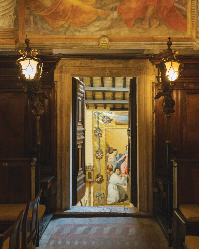 Color photo of Roman interior with ornate door flanked by large sconces opened to inner room.