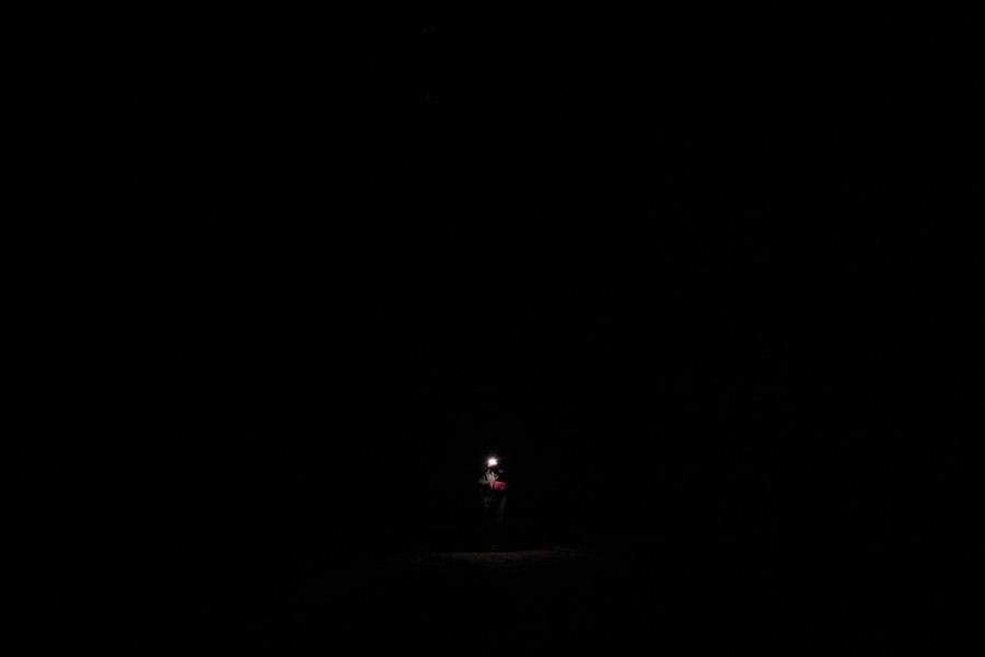 A very dark image, with only the headlamp, jacket, and purse of a walking person visible.