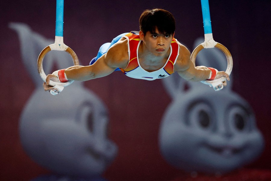 A gymnast holds a pose, lifting his body while hanging from rings.