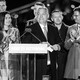 Viktor Orbán stands at a lectern surrounded by clapping, smiling people.