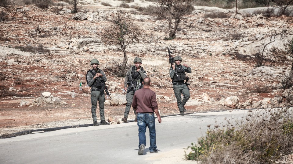 A man faces three armed Israeli soldiers on a road.