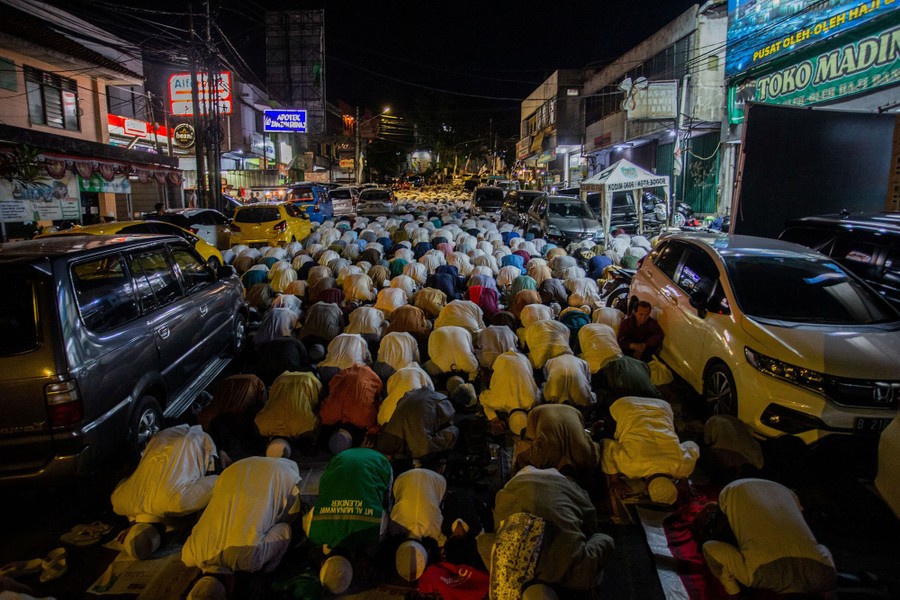 A street is filled with hundreds of people kneeling in prayer.
