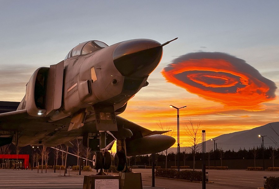 An unusual lenticular cloud behind a plane is seen during sunrise