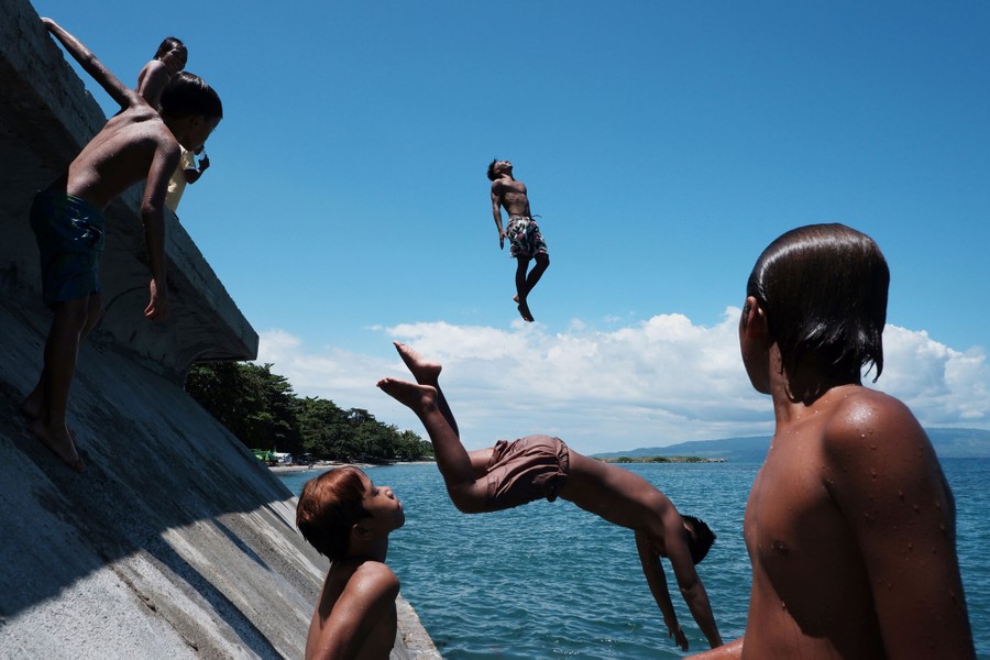 Boys and young men jump into the ocean from a seawall.