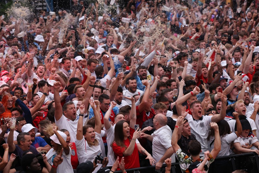 A crowd of soccer fans erupts with joy, raising their arms and tossing many beers.