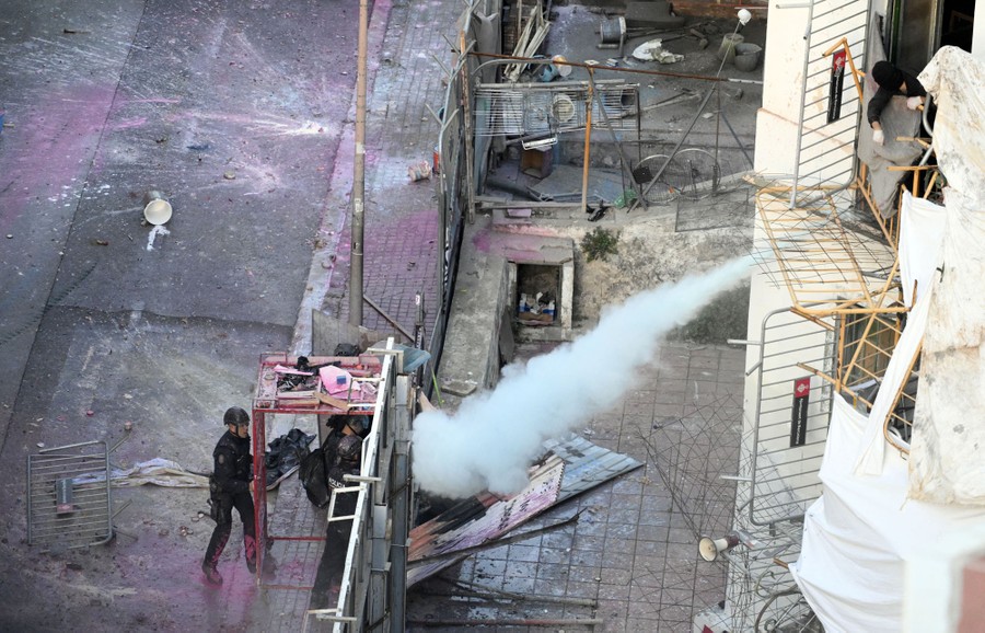 People spray fire extinguishers from an upper floor balcony, aiming down at police officers on the sidewalk below.