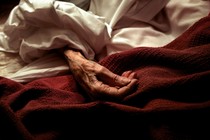 red blanket on hospital bed with an elderly hand on top