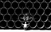 Large pipes for the Baltic Sea pipeline Nord Stream 2 are stacked in a storage area in the ferry port of Sassnitz/Neu Mukran. An employee of the responsible company Wasco crouches in front of the pipes.