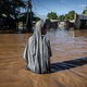 A woman wades through muddy waist-deep floodwater in an inundated residential area.