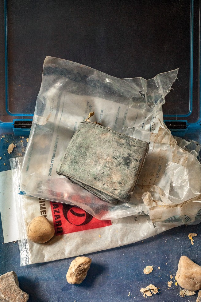 Photo of Bobby's dusty wallet on top of plastic bags, one with biohazard symbol, surrounded by several rocks