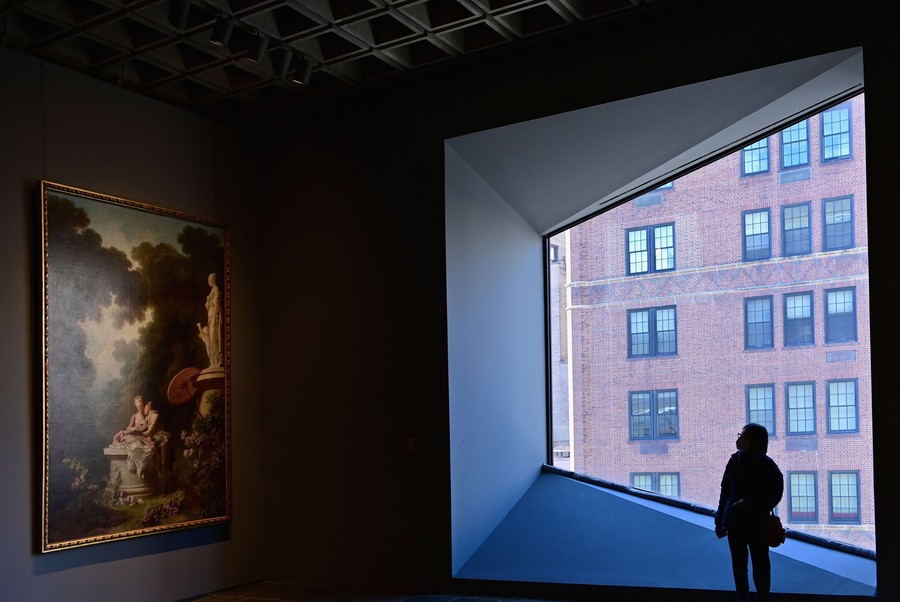 A person stands in front of a window, inside an art gallery, looking toward a large painting.
