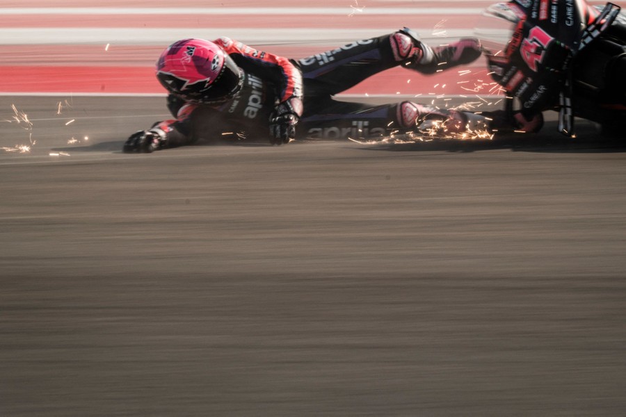 A motorcycle racer skids along the ground behind their bike after crashing.