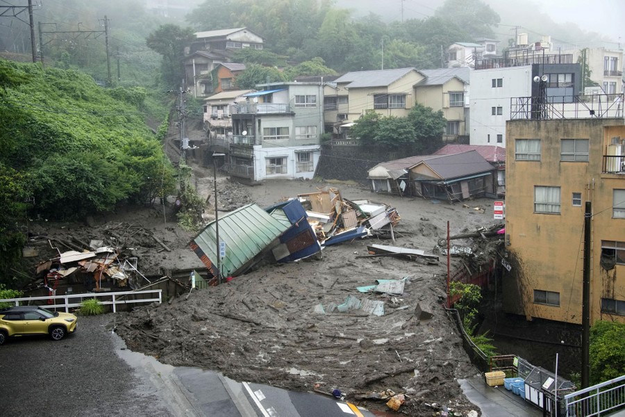 A mudslide filled with debris is seen among houses and cars.