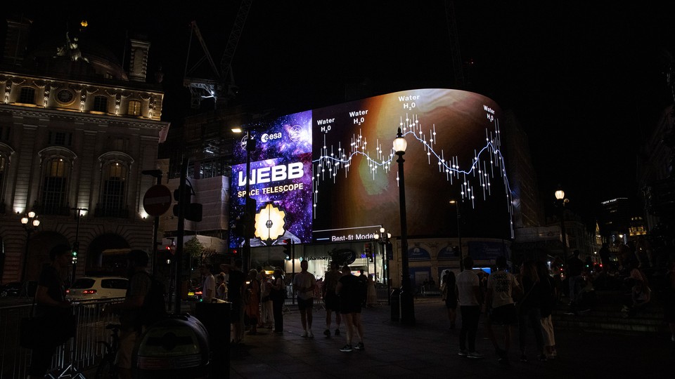 A chart from the James Webb Space Telescope is displayed on a digital billboard on a street at night.