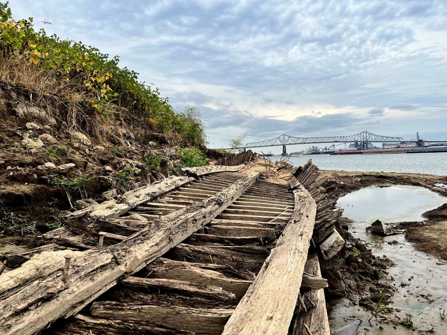 Wooden beams, parts of the wreckage of an old ship, lie on a riverbank.