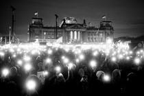 A black-and-white photo of protesters holding up lights outside the Reichstag building