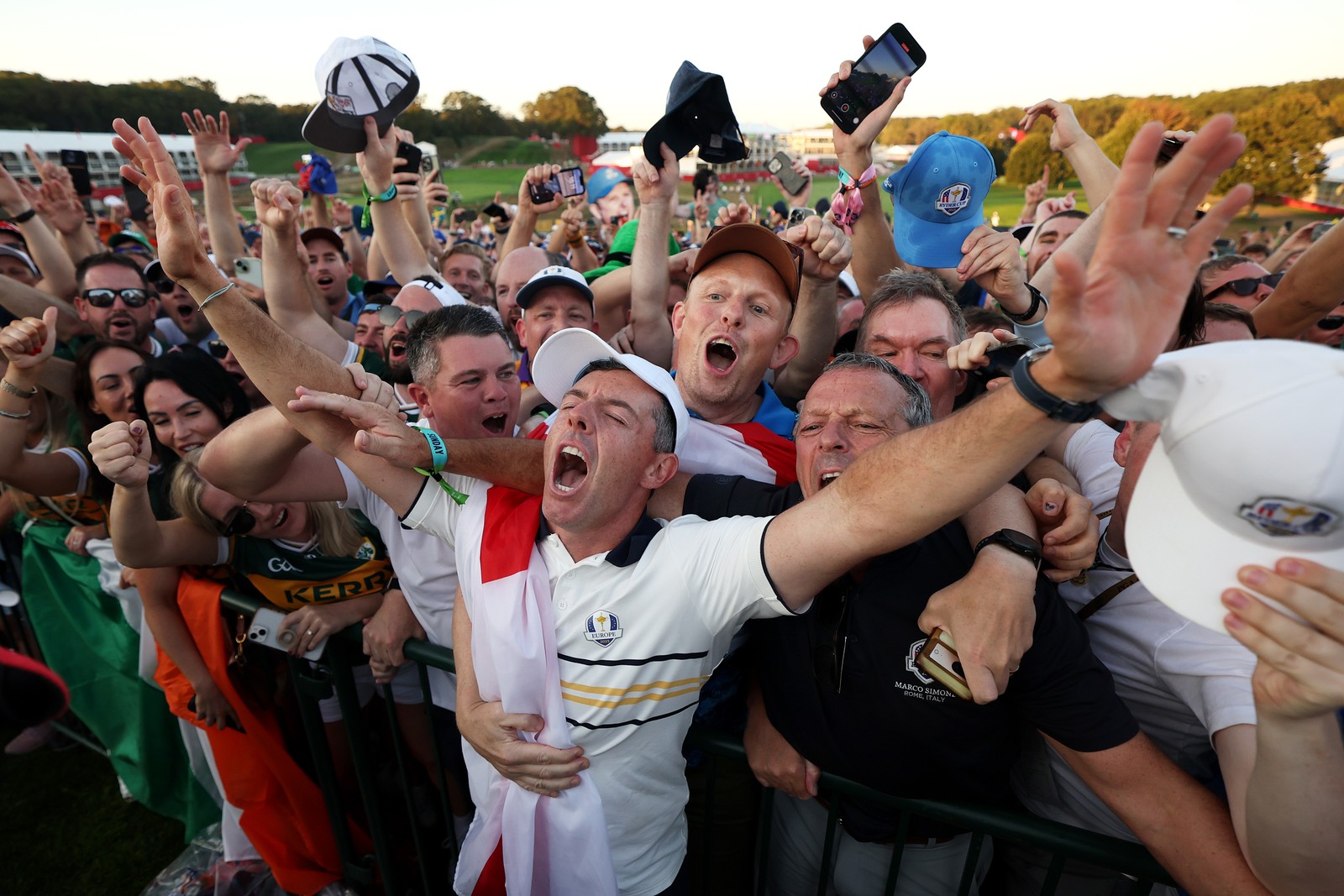 A crowd of soccer fans gather and cheer behind Rory McIlroy after a golf match.
