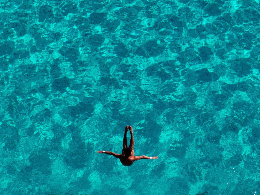 A diver, seen from above, tumbles during a dive into pool water below.