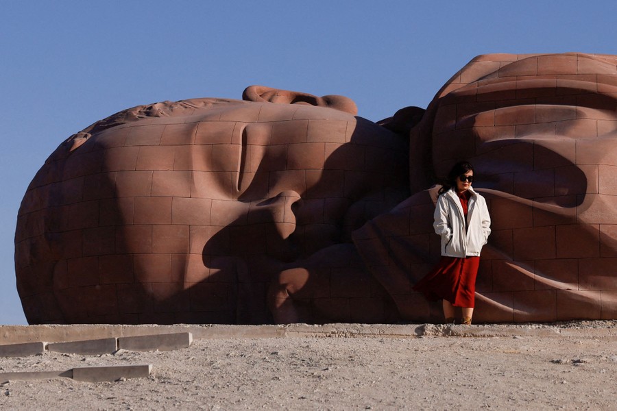 A visitor poses in front of a large sculpture of a sleeping child.