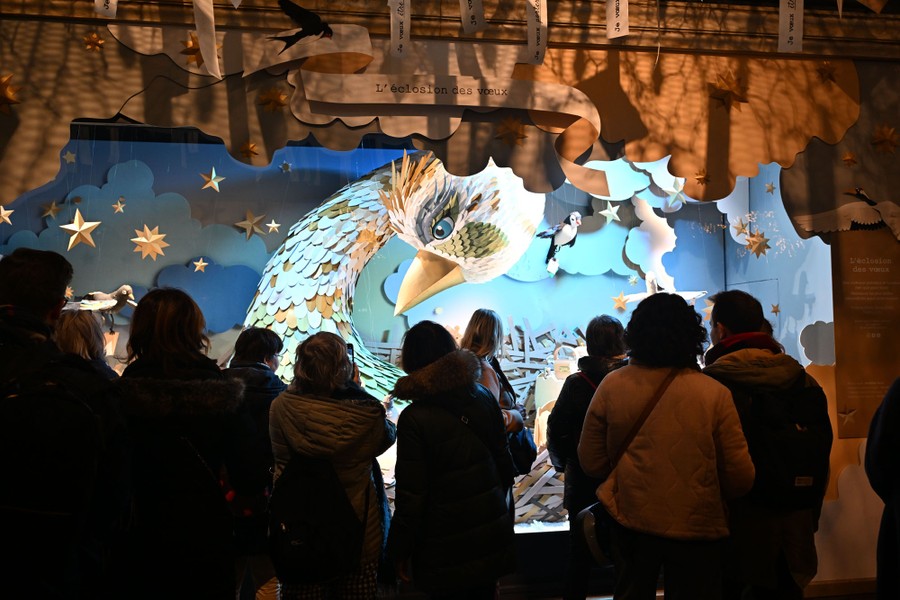 People look at a holiday window display featuring a large sculpture of a bird.