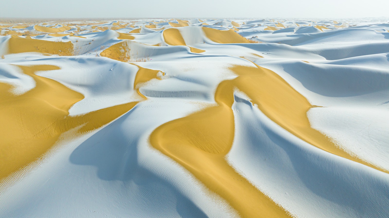 An aerial view of a field of sand dunes covered by a light dusting of snow